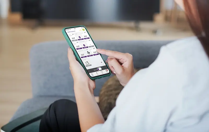 Mains tenant un smartphone ouvert sur l’application Atlantic Cozytouch, dans un salon