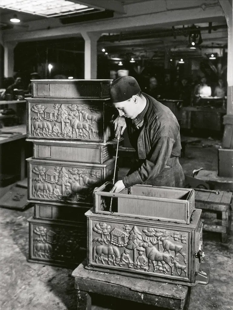 Photo noir et blanc d'un ouvrier assemblant des poêles en fonte à reliefs dans un atelier