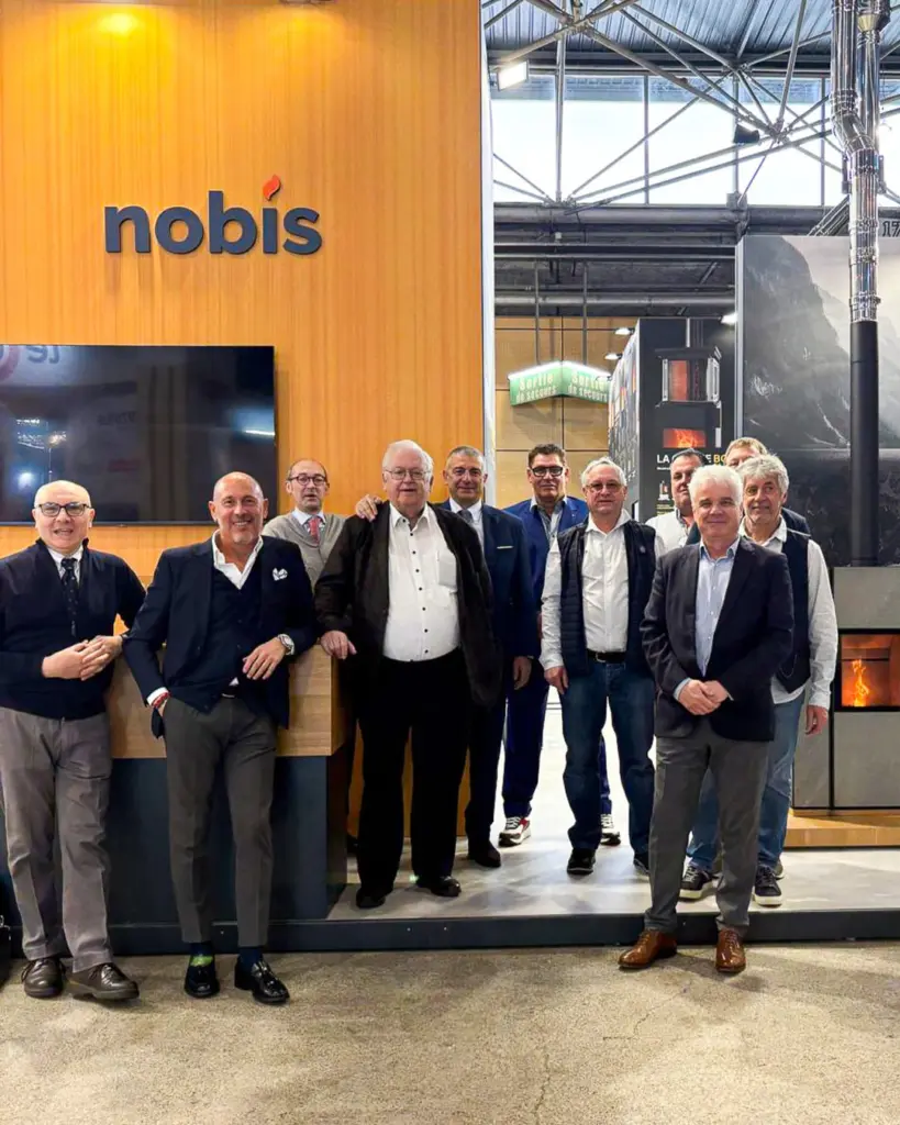 Une dizaine d'hommes posent devant le stand Nobis à mur orange, dans un hall de salon