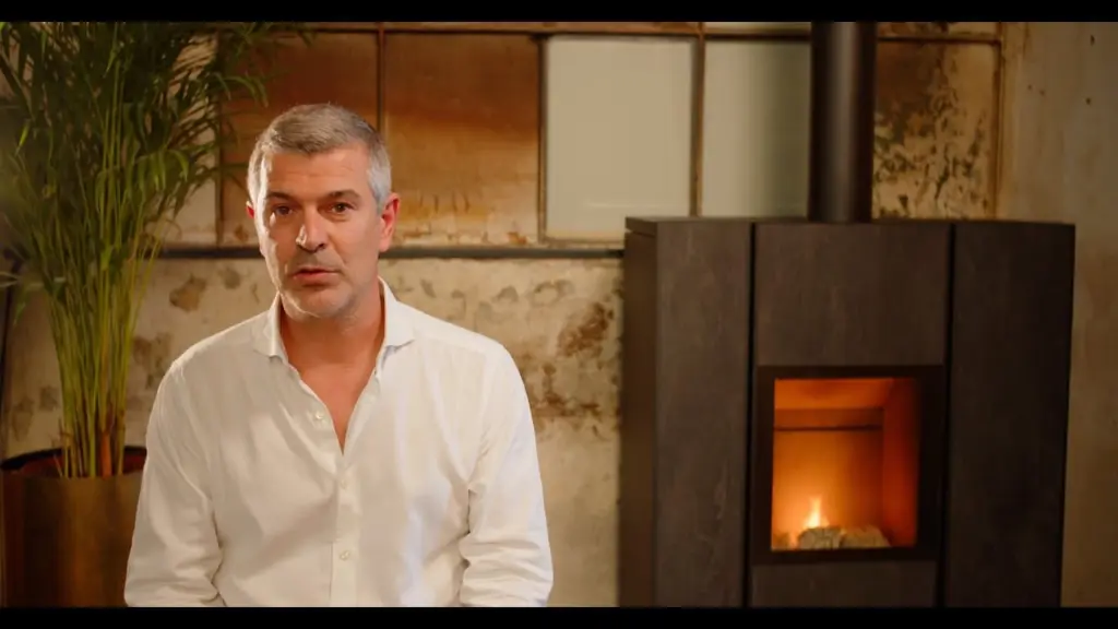 Diego Ravelli, en chemise blanche, parle face caméra devant un poêle Nobis allumé