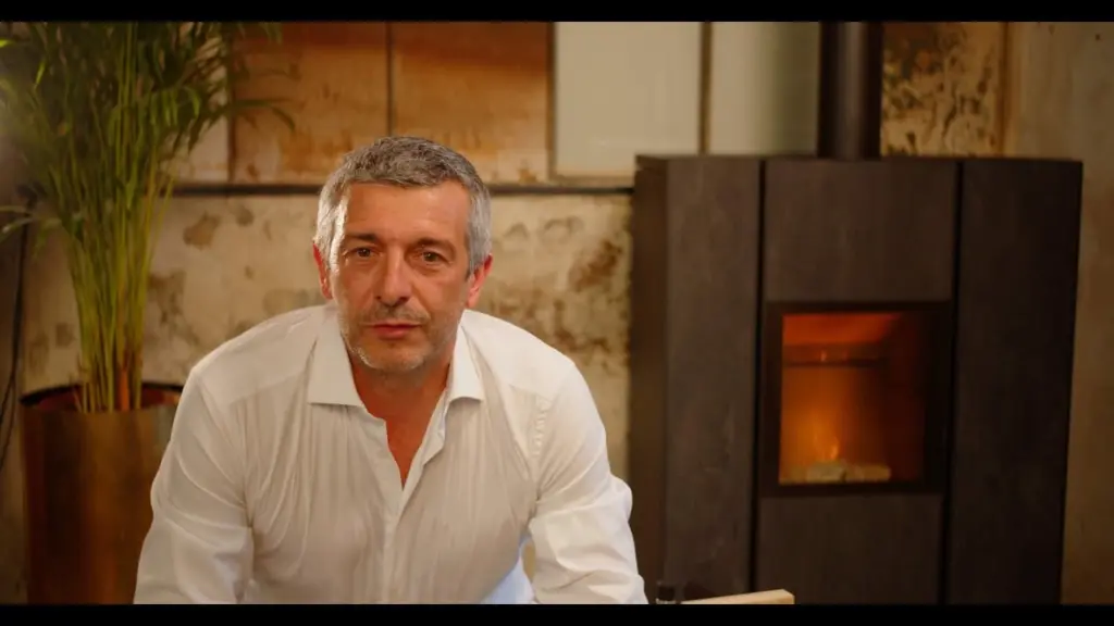 Stefano Ravelli, en chemise blanche, assis devant un poêle Nobis allumé