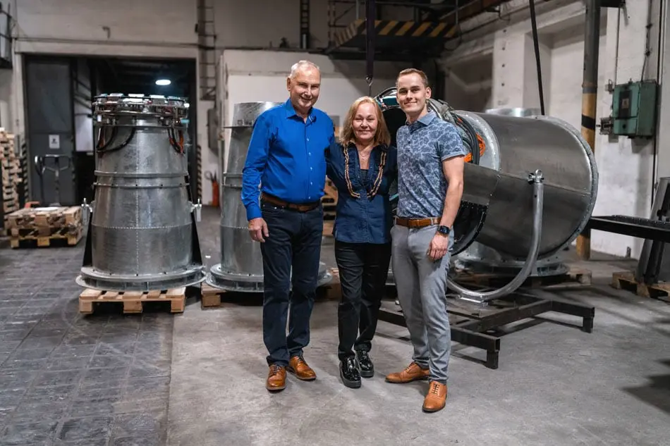Trois membres de la famille Hein debout dans un atelier de l'usine, entre des pièces métalliques