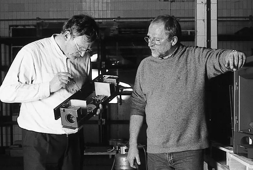 Photo noir et blanc de deux hommes dans un atelier, l'un examinant une pièce métallique d'appareil de chauffage