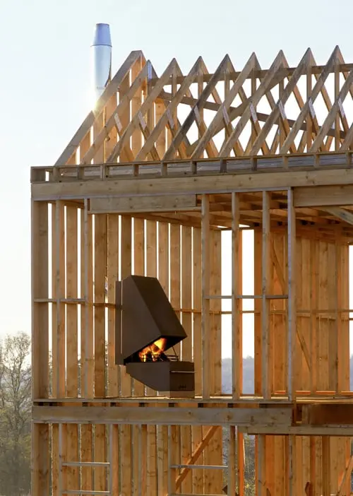 Poêle suspendu Stûv 60 allumé, au milieu d'une charpente de maison en bois