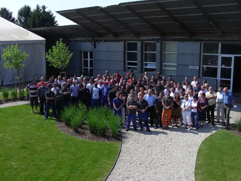 Photo de groupe d'une centaine de salariés devant un bâtiment industriel marqué Accueil