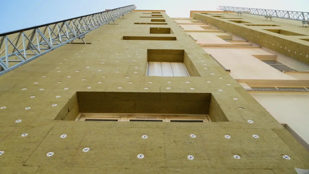 Façade d'immeuble vue d'en bas, couverte de panneaux de laine de roche jaune fixés par des chevilles blanches, autour des fenêtres, avant l'enduit