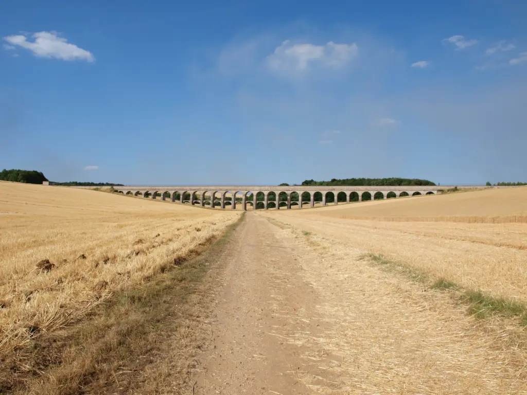 L’aqueduc de la Vanne à Cuy, ses arcades à l’horizon au bout d’un chemin entre les champs moissonnés.