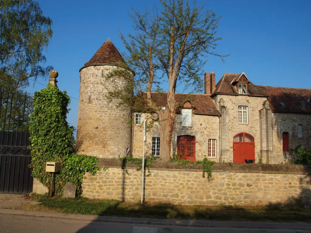 Le château de La Chapelle-sur-Oreuse, sa tour ronde et ses portes rouges derrière un mur de pierre.