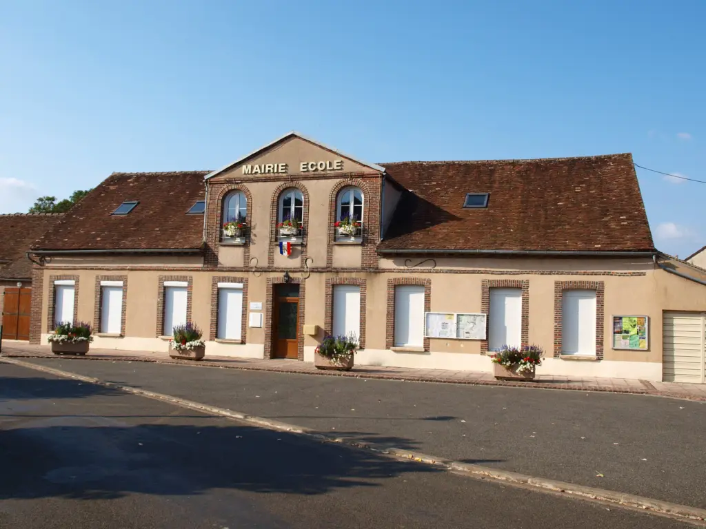 La mairie-école de Noé, façade de brique et de pierre fleurie, au bord de la rue.