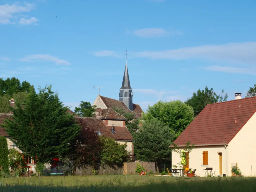 Guerchy, commune déléguée de Valravillon : le clocher pointu de l’église au-dessus des toits et des arbres.